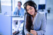 Portrait of attractive customer support service worker woman taking notes while listening customer over headset. Female operator at office.