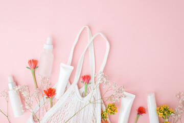 skincare and cosmetic product on pink pastel background with flowers and a fabric bag. Beauty and lifestyle concept with copy space, flatlay. 
