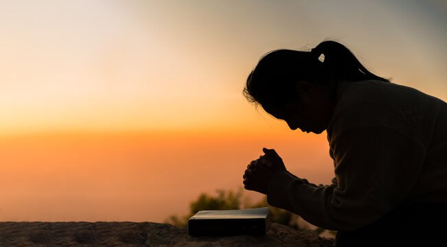 Silhouette of woman kneeling down praying for worship God at sky background. Christians pray to jesus christ for calmness. In morning people got to a quiet place and prayed. Banner with copy space.