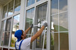 Professional window installer outside the building installs a protective insect net on large plastic window. Working man holds a mosquito net in his hands, compares the size with window