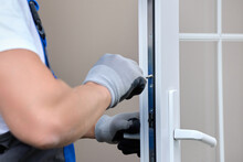 Close-up Professional Craftsman In Gloves Repairs The Lock On The White Plastic Door. Professional Glazing And Installation Of Plastic Windows And Door Systems