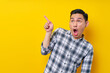 © Bangun Stock Photo - Surprised young handsome Asian man 20s wearing a plaid shirt pointing a finger at the advertising area isolated on yellow background. People lifestyle concept