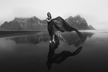 Wall Mural - Happy lady wrapped with chiffon on beach monochrome scenic photography. Picture of person with hills on background. High quality wallpaper. Photo concept for ads, travel blog, magazine, article