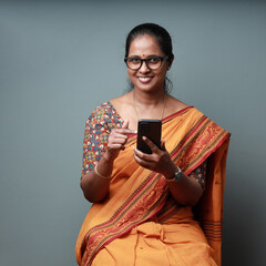 Wall Mural - Portrait of a happy Indian woman wearing Sari holding a mobile phone in hand 