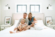 © Cavan Images - Portrait of a family sitting together on a bed making silly faces