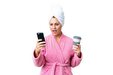 Canvas Print - Middle age caucasian woman in a bathrobe over isolated background holding coffee to take away and a mobile