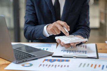 Wall Mural - Asian businessman working in the office, calculating financial reports, organizing paperwork using a laptop and calculator as an aid.management concept accounting.