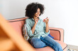 © Vadim Pastuh - Focused woman sitting on the sofa at home and holding smartphone. Multiracial girl reading news online, spending leisure time in social networks. Female texting and chatting online