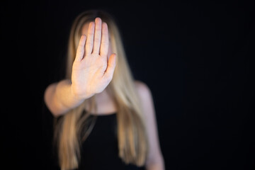 Woman showing hand stop sign to campaign against gender violence and pain. Hand raised to dissuade for self harm awareness, stop abusing and bullying. Human rights. Black background with copy space.