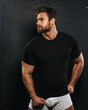 Bearded handsome man in black shirt and white boxers at black background. Sexy muscled guy in casual underwear in studio. Male fitness model posing in relaxing outfit.