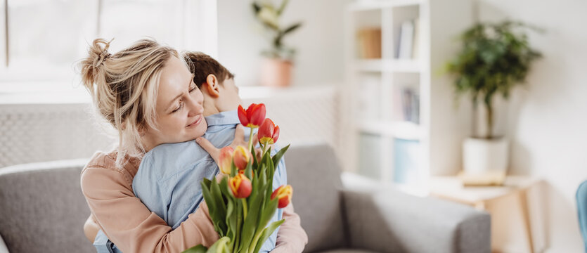 Fototapete - Cute boy sitting on the sofa with mom and giving a bouquet of tulips to her.