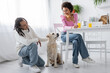 © LIGHTFIELD STUDIOS - Smiling african american woman holding croissant and looking at boyfriend and labrador at home.