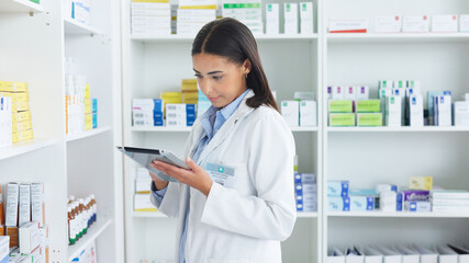 A young female pharmacist stocktaking in a dispensary using a tablet. Doctor preparing prescriptions and medication at clinic or pharmacy. Healthcare professional sorting medicine with digital device