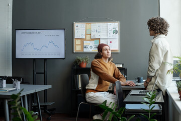 Fototapete - Young intercultural economists in casualwear discussing changes on stock market or consulting about cryptocurrency analysis by workplace
