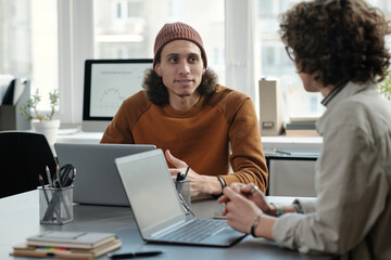 Leinwandbilder - Young confident businessman in casualwear looking at female colleague during discussion of working plan points by workplace in office