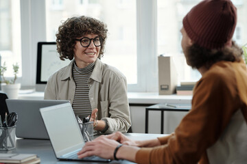 Leinwandbilder - Young confident businesswoman looking at male colleague during discussion of online data or consulting about working point