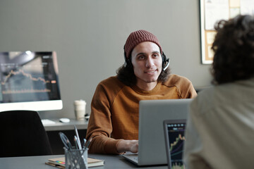 Leinwandbilder - Young businessman with headset looking at female colleague during communication in office while both sitting in front of laptops