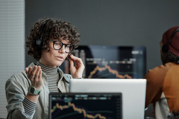 Poster - Young confident operator in headset explaining something to online client while sitting by workplace in front of laptop and looking at screen