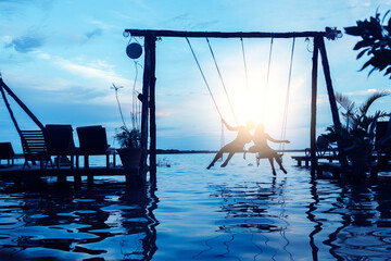 Silhouette of couple on rope swings on the beach