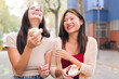 female couple laughing and having fun while sharing some sweet buns sitting in a city park, concept of friendship and love between people of the same sex