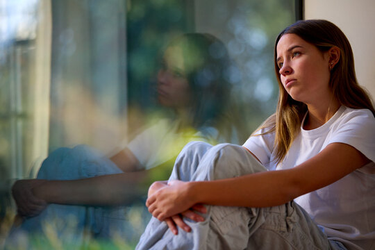 depressed teenage girl sitting looking out of window at home