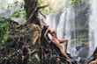 Wet gorgeous woman posing on the roots tree in the jungle beside mighty Phnom Kulen waterfall