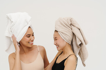 Wall Mural - Two beautiful women smiling at each other while posing isolated over white wall