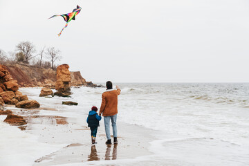 Wall Mural - Back view of father and his son playing with kite on the beach