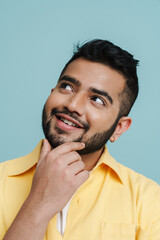 Wall Mural - Pensive indian man touching his chin while posing isolated over blue background