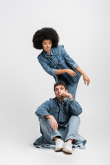 Wall Mural - full length of curly african american woman standing behind man in denim outfit and sneakers on grey.