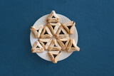 Fototapeta Łazienka - Happy Purim carnival decoration concept made from Hamantaschen or hamans ears cookies on the plate on blue background. Hebrew, jewish holiday celebration composition in shape of Star of David 