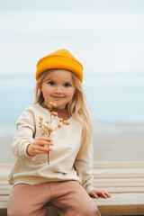 Wall Mural - Child girl walking outdoor on the beach kid 4 years old in yellow hat family travel vacations autumn season