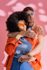 Wall Mural - Stylish brunette man hugging african american woman on pink background with shadow.