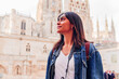 © Dani D.G - Low angle of smiling young Hispanic woman in denim jacket with backpack and photo camera looking up against Cathedral of Saint Mary of Burgos, Castile and Leon