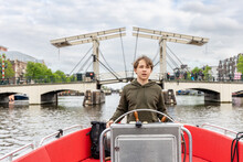 A Boy At The Wheel Of A Boat On A Canal In Amsterdam