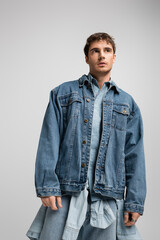 young man in denim jacket posing and looking away isolated on grey.