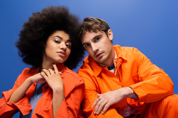 Wall Mural - Portrait of stylish interracial couple in bright jackets isolated on blue.