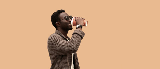 Wall Mural - Portrait of happy young african man drinking coffee walking isolated on brown background