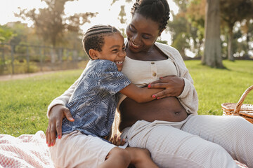 Happy african mother hugging son at city park - Pregnant woman with child outdoor