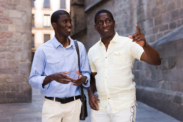 Wall Mural - Positive african american men talking and pointing finger at the old street