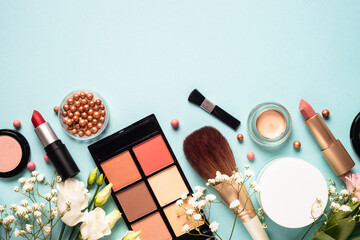 Fototapete - Make up professional, Cosmetic products on blue background. Cream, powder, shadow, brushes with green leaves and flowers. Top view with copy space.
