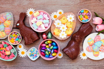 Wall Mural - Easter candies. Above view table scene over a wood background. Chocolate bunnies, candy eggs and an assortment of sweets.