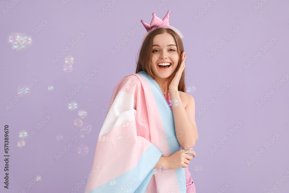 Young woman in crown with transgender flag and soap bubbles on lilac background