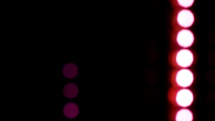 Wall Mural - Vertically falling magenta blur light dots. Magenta bokeh with reflexes fall down on a black background. Defocused light circles in rows. Loop 4K video.