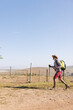 © Wavebreak Media - Side view of african american senior man with hiking poles walking on land against clear sky