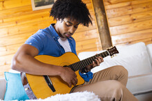 Happy African American Man Spending Time In Log Cabin Playing Guitar