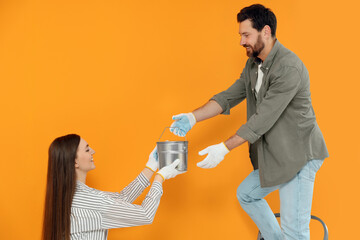 Canvas Print - Woman giving man can of paint near orange wall. Interior design