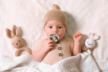 Wall Mural - Cute newborn baby with pacifier and toys on white knitted plaid, top view