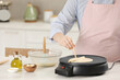 © New Africa - Woman cooking delicious crepe on electric pancake maker at white marble table in kitchen, closeup
