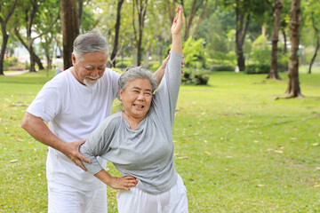 Asian senior couple practice yoga excercise, tai chi tranining, stretching and meditation together with relaxation for healthy in park outdoor after retirement. Happy elderly outdoor lifestyle concept